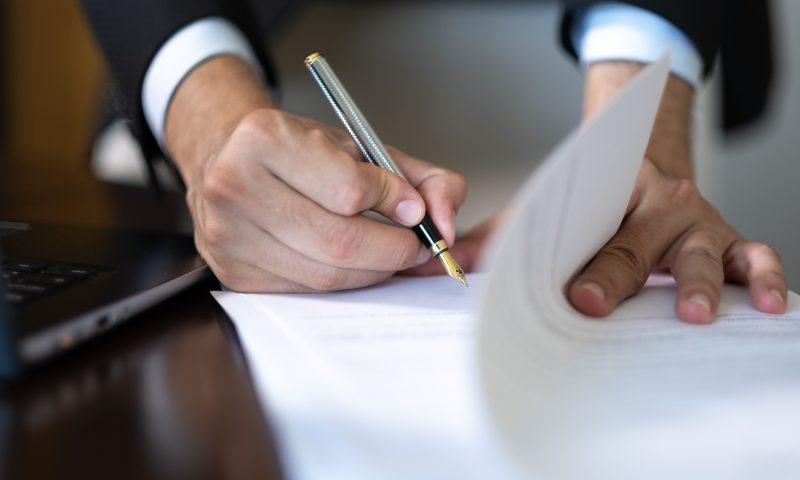 Close-up of hands of unknown businessman in suit signing official document Lawyers helping with claims