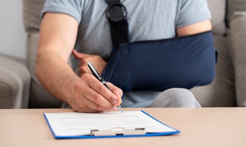 handicapped man with sling signing contract at home Front view of a handicapped man with sling signing contract at home
